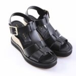 Black platform wedge sandals with braided jute heel and wide leather straps, gold buckle ankle strap.