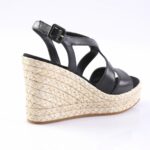 Black leather wedge sandal with a braided jute platform and ankle strap in an open-toe design.