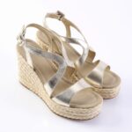 Gold metallic wedge sandals with a braided espadrille platform and multiple straps on a white background.