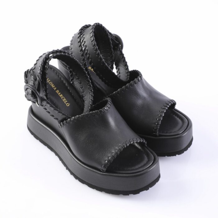 Black platform sandals with thick soles and hand-stitched edges; open toe and ankle strap visible on white background.