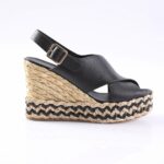 Black leather wedge sandal with an ankle strap and gold buckle on a braided jute platform.