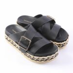 Black platform sandals with crisscross straps and gold-tone buckles, featuring a braided jute-sole edge.
