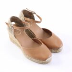 Tan leather espadrille wedge sandals with ankle strap and braided jute sole, on a white background.