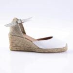White espadrille wedge sandal with an ankle strap and braided jute heel on a white background.