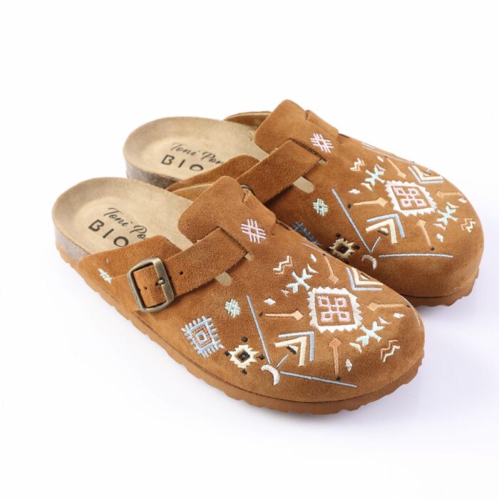 Brown suede slip-on clogs with decorative white and blue embroidery and an adjustable buckle strap, shown on a white background.]