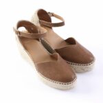 Brown leather espadrille wedge sandals with ankle straps and a woven jute sole on a white background.