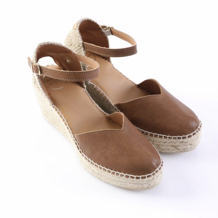 Brown leather espadrille wedge sandals with ankle straps and a woven jute sole on a white background.