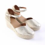 Gold metallic espadrille wedge sandals with ankle strap and braided jute sole on a white background